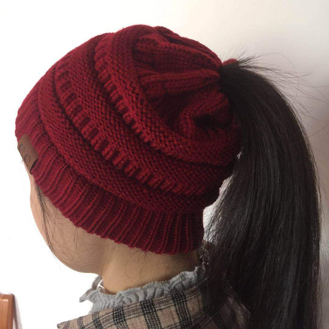 Red knitted beanie worn by a person with a ponytail on a plain background
