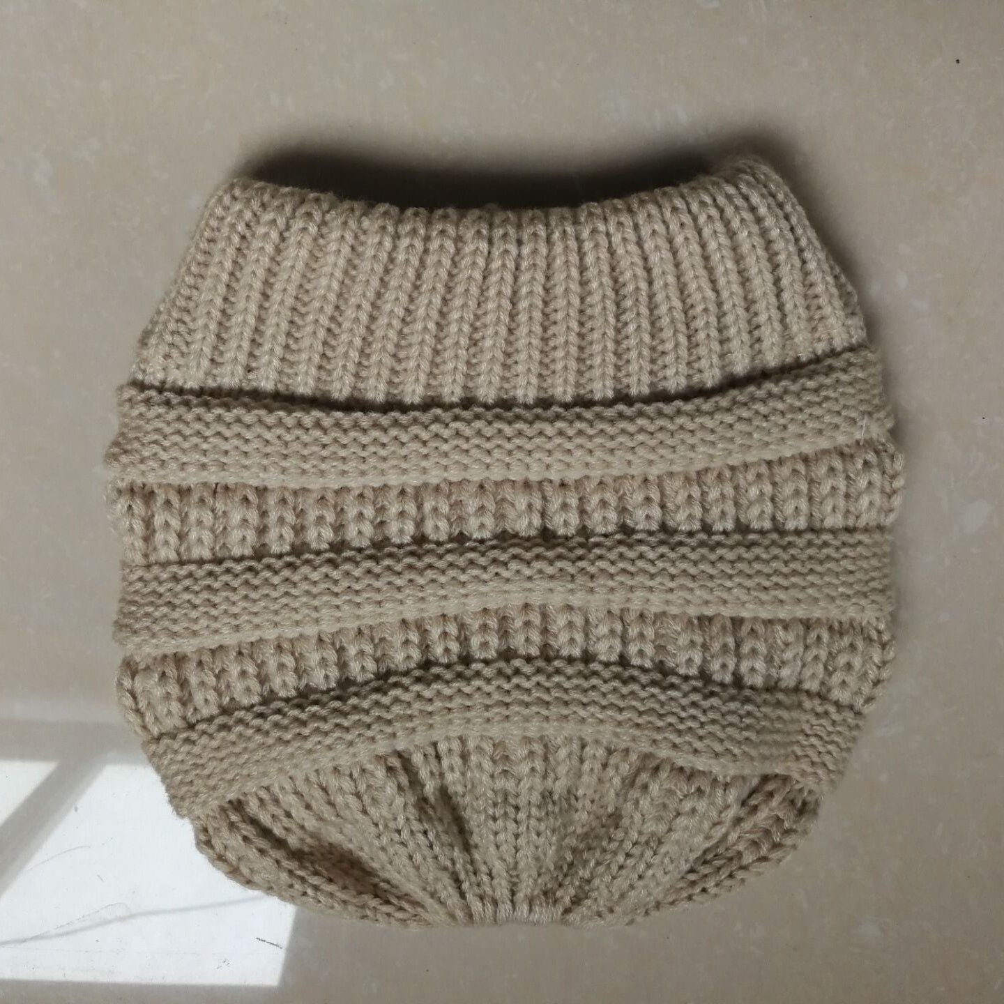 Knitted beige ponytail knitted hat on a neutral background