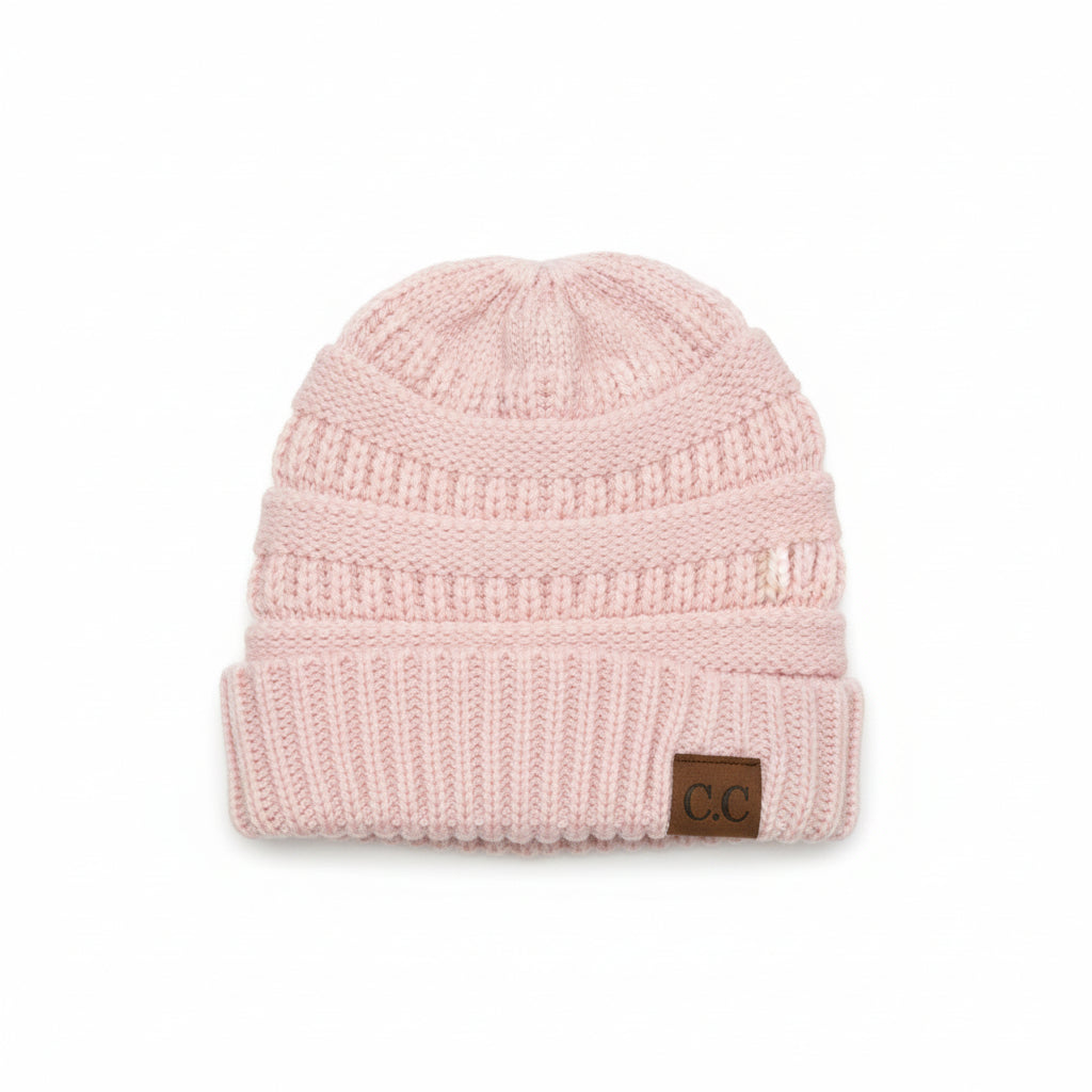 Knitted pink beanie with a brand label on a wooden surface
