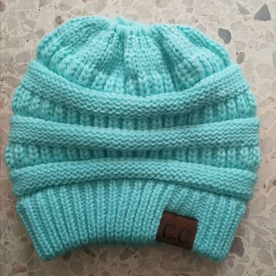 Turquoise knit beanie with a brown label on a textured surface