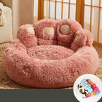 Fluffy pink paw-shaped pet bed on a carpeted floor with a window in the background.